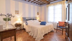 Une chambre à coucher comprenant un lit, des tables de chevet, une chaise, une fenêtre avec des rideaux et un plafond en bois.