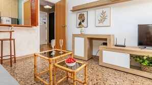 Un salon moderne avec une table à plateau en verre, deux fauteuils, un meuble en bois, un téléviseur et des œuvres d’art accrochées au mur.