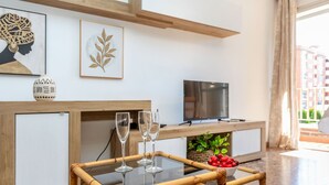 Un salon moderne avec une table à plateau en verre, deux verres à vin, un bol de cerises, un téléviseur et des œuvres d’art accrochées au mur.