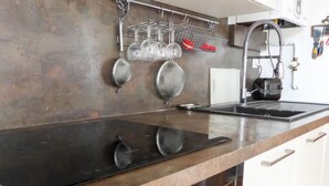 A kitchen with a black induction cooktop, stainless steel pots, a hanging rack with glasses, and a coffee machine. - Demeures de Maignon by Interhome (Anglet)