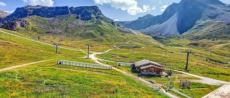 Un paysage montagneux avec un petit bâtiment, une voie ferrée et un télésiège.