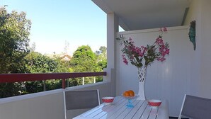Un balcón con una mesa y sillas blancas, un florero con flores y una barandilla roja.