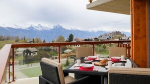 Ein Balkon mit Korbmöbeln, einem Tisch für zwei Personen und Blick auf die Berge.