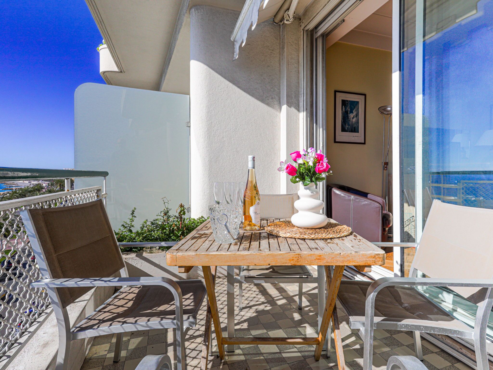 A balcony with a table, chairs, a bottle, and a vase with flowers.