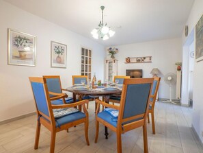 A dining area with a round table, four chairs with blue cushions, a chandelier, and wall-mounted artwork. - Les Troenes by Interhome (Fréjus)