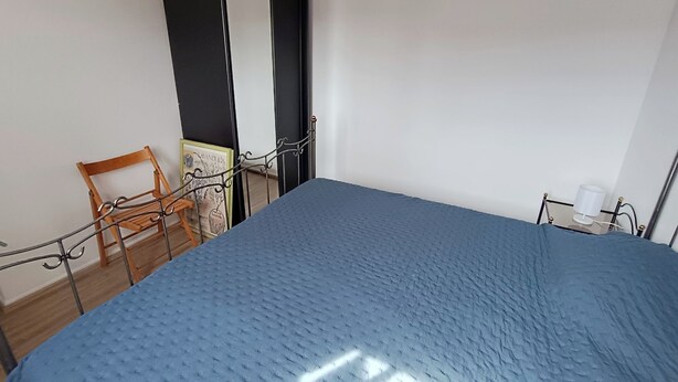 A bedroom with a bed, a chair, a small table with a lamp, and a door. - Les Troenes by Interhome (Fréjus)