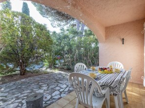 An outdoor patio with a stone floor, white plastic chairs, and a table set with fruits and a bowl.