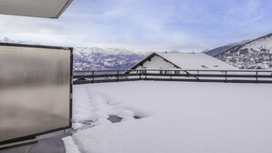 En snötäckt balkong med utsikt över snöklädda berg och en liten byggnad i bakgrunden.