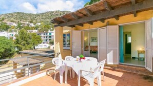 A covered outdoor patio with a table and chairs, a view of the surrounding area, and a building with a sloped roof. - Velazquez by Interhome (Roses)