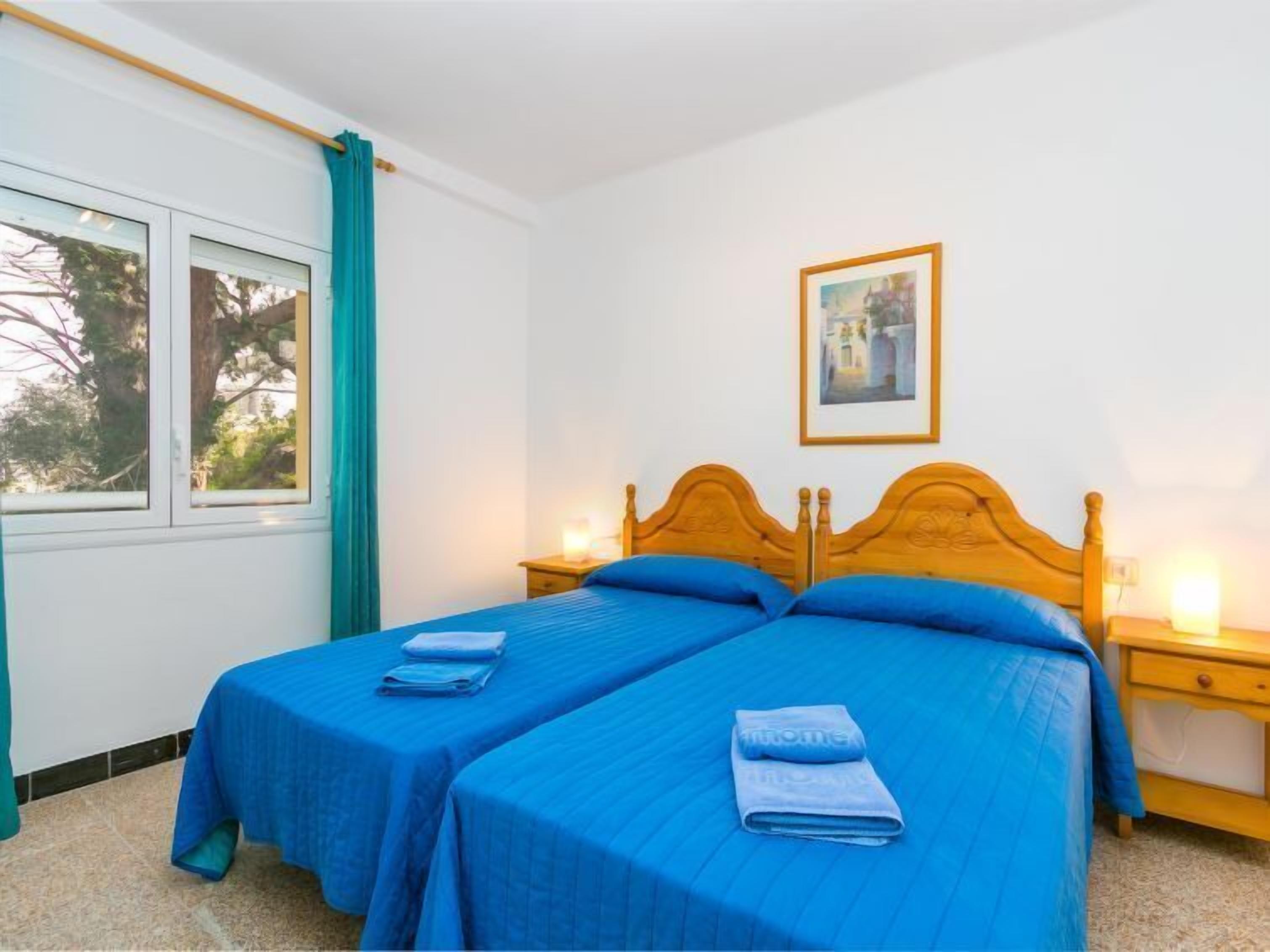 A double room with two single beds, a wooden headboard, a bedside table with a lamp, and a window with curtains.