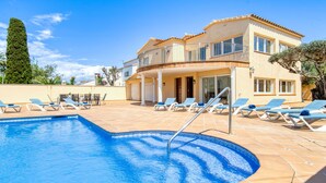 Un espace aménagé au bord de la piscine, comprenant une piscine, des chaises longues et un bâtiment à deux étages doté de balcons.