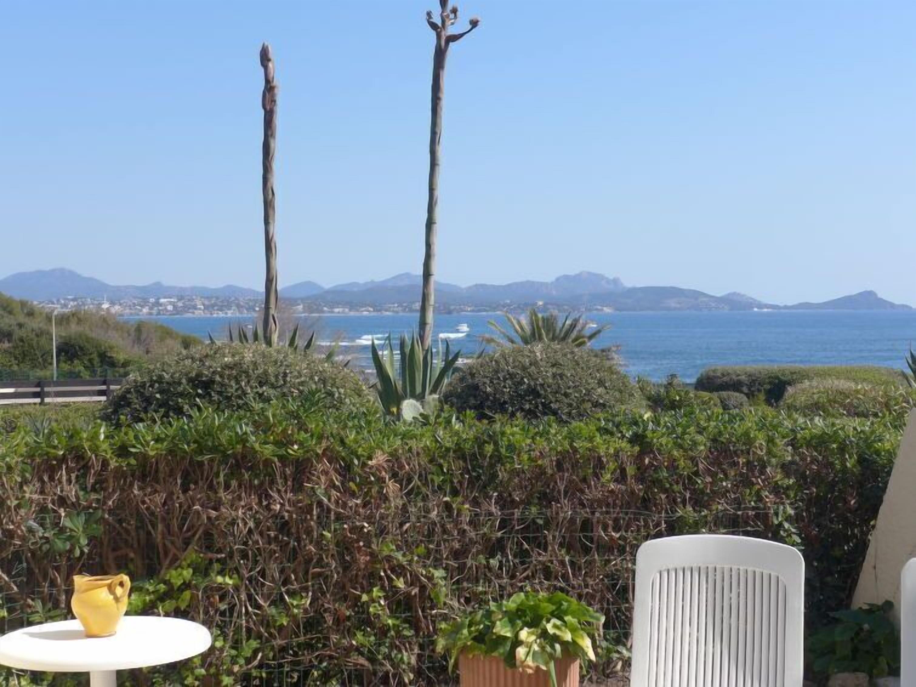 Eine Terrasse mit Blick auf das Meer, ein Tisch mit einem gelben Blumentopf und ein weißer Stuhl.