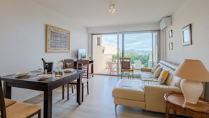 Een moderne woonkamer met een eethoek, een bank, een televisie en een balkon met uitzicht op de stad.