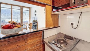 A kitchen with wooden cabinets, a stove, and a window with a view of a snowy landscape. - Rond Point des Pistes (Val Claret) by Interhome (Tignes)