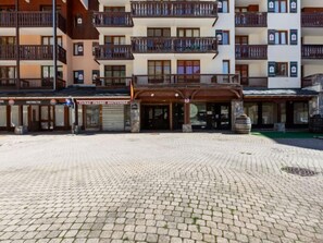 A hotel entrance with a cobblestone plaza, multiple balconies, and a sign for a souvenir shop.