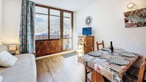 A room with a large window, a wooden desk, a television, and a dining table set for four. - Rond Point des Pistes (Val Claret) by Interhome (Tignes)