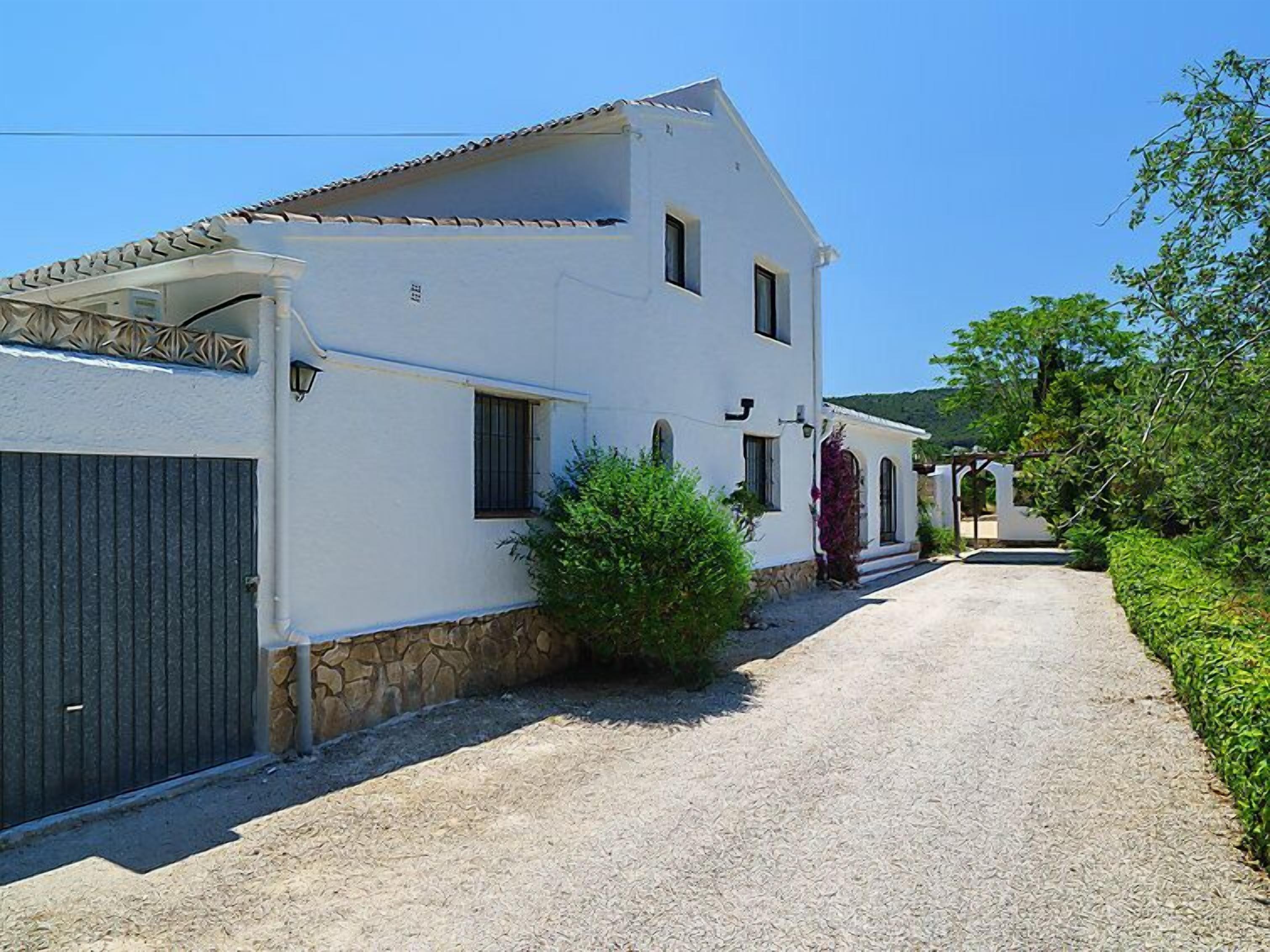 Un bâtiment blanc à deux étages, avec des fondations en pierre, une allée gravillonnée et un portail métallique sur le côté gauche.