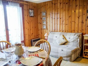 A wooden-paneled room with a dining table set for two, a sofa, and a small wooden shelf.