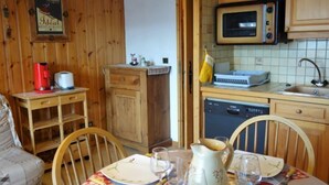 Una cocina acogedora con armarios de madera, microondas, cafetera y una mesa de comedor para dos.