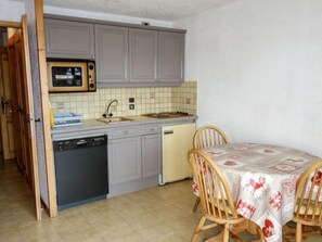 A compact kitchen with grey cabinets, a microwave, a sink, and a dishwasher. There is a dining table with chairs and a tablecloth.