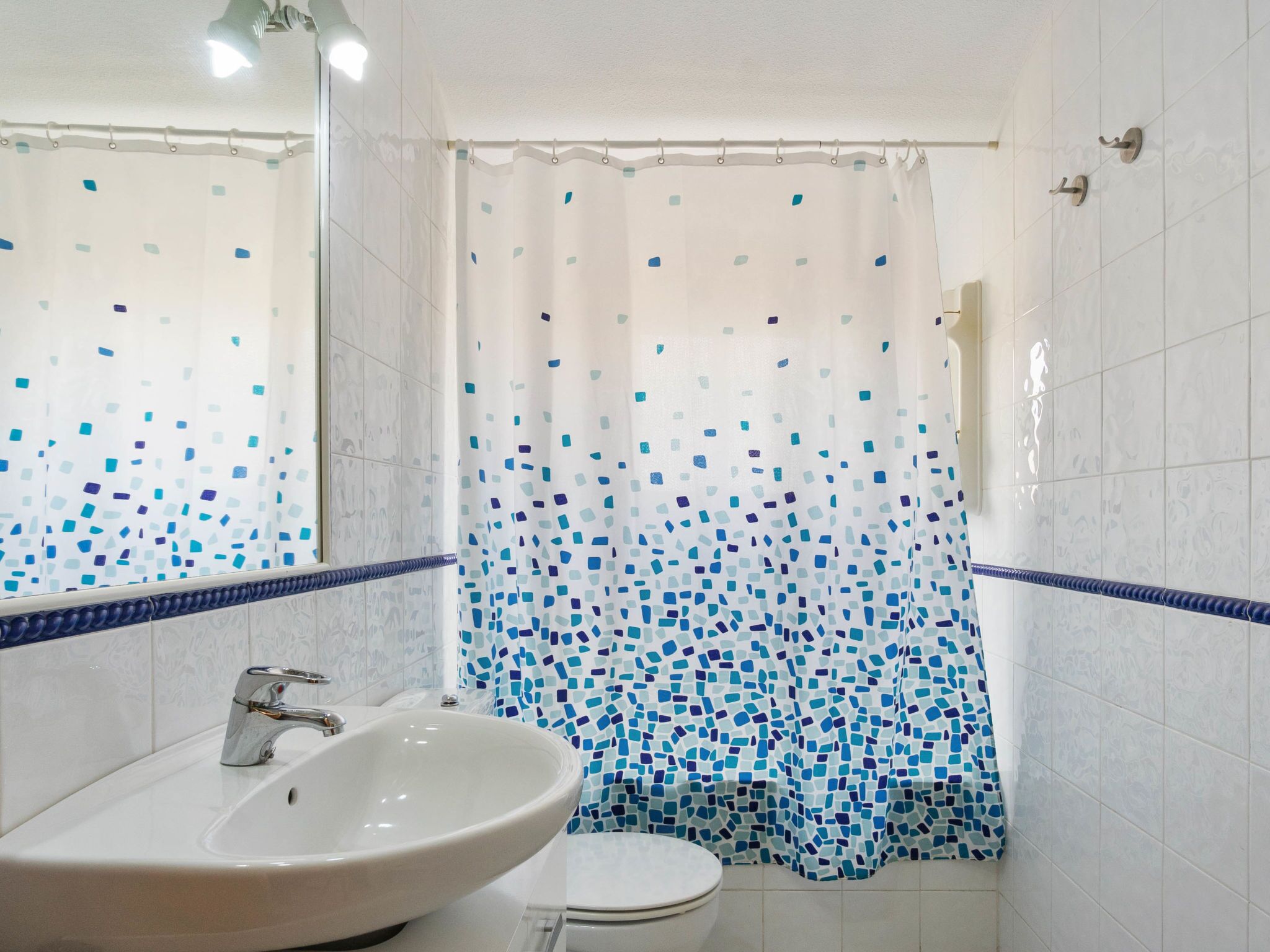 Un baño con un lavabo blanco, un inodoro y una cortina de ducha con motivos de mosaico.