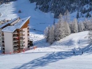 Un hôtel à plusieurs étages doté de balcons, situé sur une pente enneigée, avec des pistes de ski en arrière-plan.