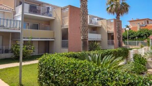 A residential building with multiple balconies, a well-maintained garden with palm trees, and a clear blue sky. - Les Flots Cypriano by Interhome (Saint Cyprien)