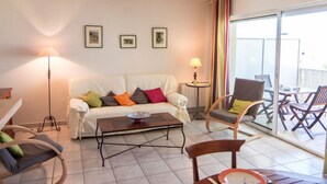 A cozy living room with a white sofa, colorful cushions, a coffee table, and a dining area with chairs and a table. - Les Flots Cypriano by Interhome (Saint Cyprien)