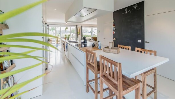 Une cuisine moderne avec un îlot central, des chaises en bois et un mur recouvert d’un tableau noir.