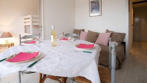 A dining area with a table set for two, a bottle of wine, and a framed picture on the wall.