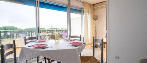 Comedor con mesa dispuesta para cuatro personas, ventanas amplias y vistas a zonas verdes.