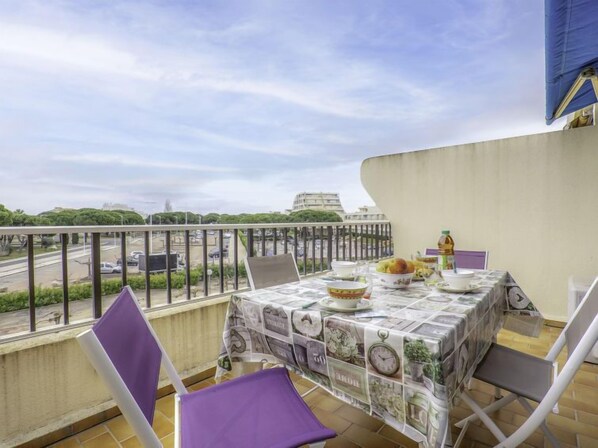 A balcony with a table set for dining, chairs, and a view of a cityscape. - Les Jardins du Port by Interhome (Port Camargue)