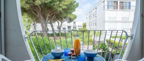 A balcony with a table set for two, a bottle of orange juice, and two bowls.