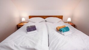 Una cama doble con ropa blanca, dos mesitas de noche con lámparas y toallas sobre la cama.