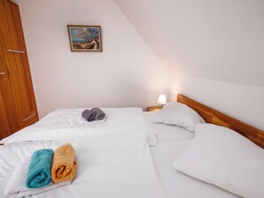Una cama individual con ropa blanca, un cabecero de madera y una mesita de noche con lámpara.