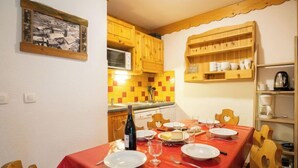 A dining area with a red tablecloth, wooden chairs, and a wine bottle. - Balcons d'Olympie 204 - A by Interhome (Les Menuires)