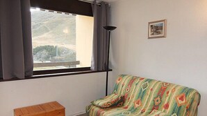 Een kamer met een bed, een houten bankje, een raam met gordijnen, een vloerlamp en een lijst met een afbeelding aan de muur.