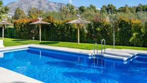 A swimming pool with clear blue water, surrounded by a well-maintained lawn and tropical plants. - Los Naranjos Singles by Interhome (Marbella)