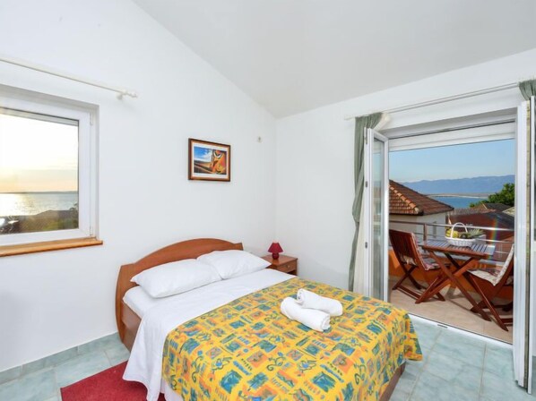 Um quarto com cama, mesa de cabeceira, janela e varanda com mesa e cadeiras.