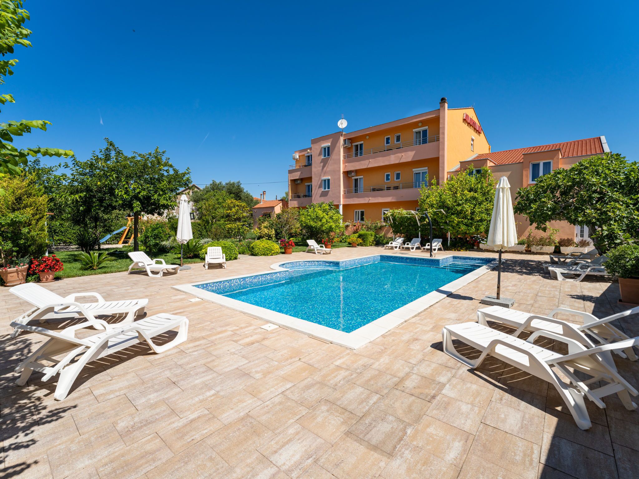 A swimming pool with lounge chairs, surrounded by a garden and a building with balconies.