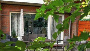 A patio with a brick wall, a glass door, and a seating area with chairs and a table. - Muschelweg by Interhome (Norddeich)