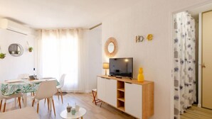Una sala de estar moderna con comedor, un televisor sobre un soporte de madera y una mesita con tazas.
