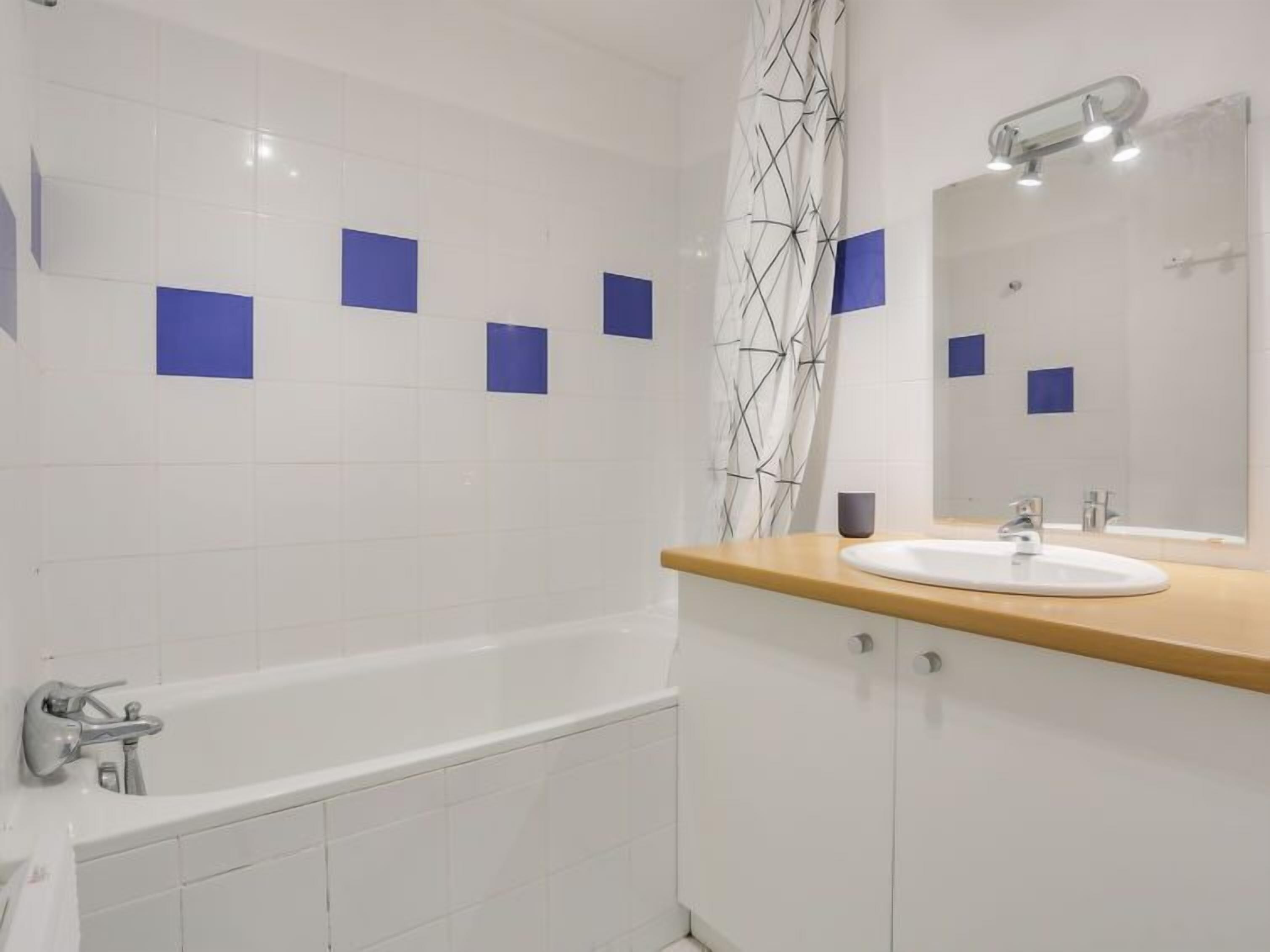 A modern bathroom with a white bathtub, a wooden vanity with a sink, and a large mirror.