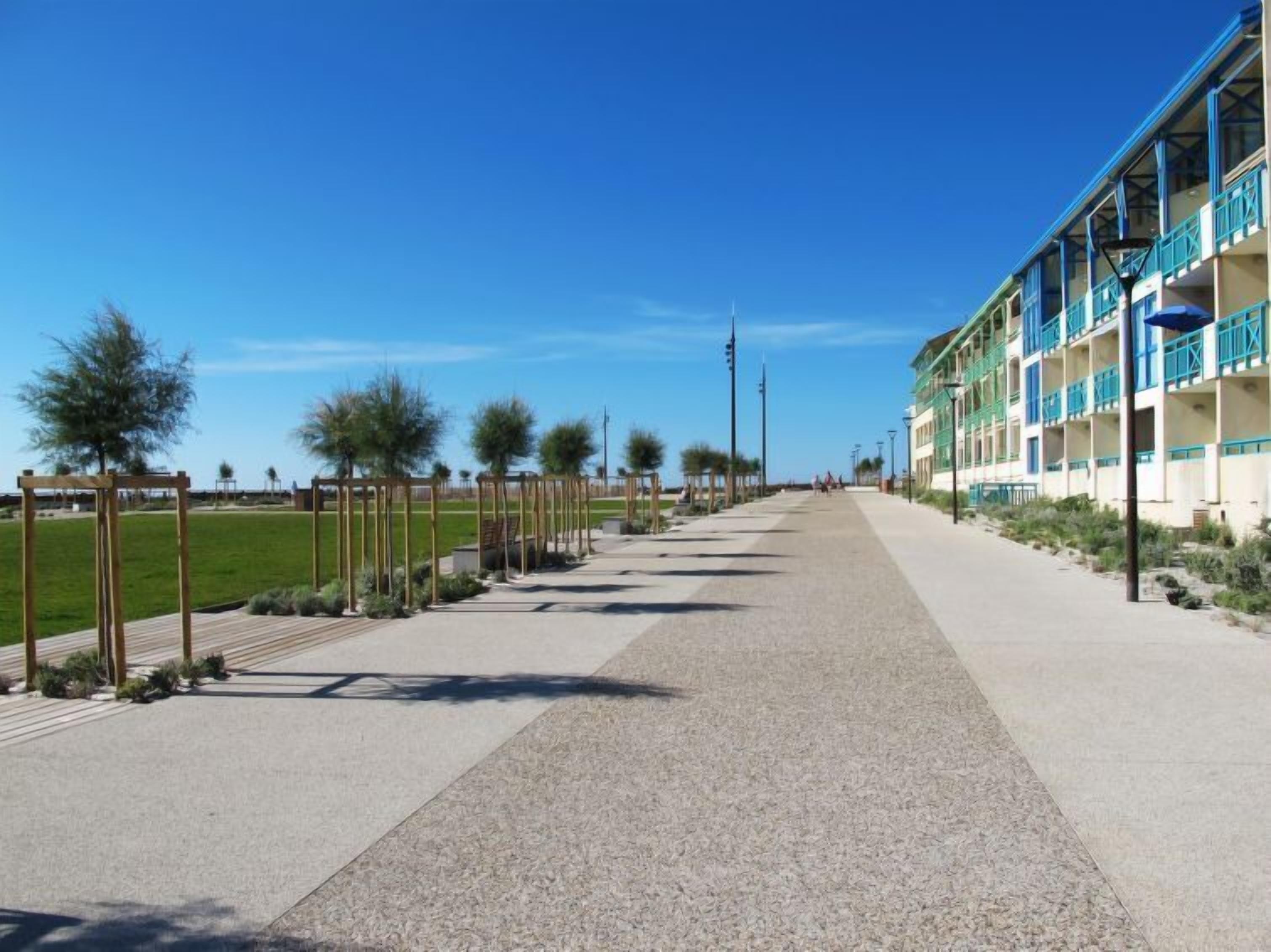 A pathway leading to a building with multiple balconies and a clear sky.