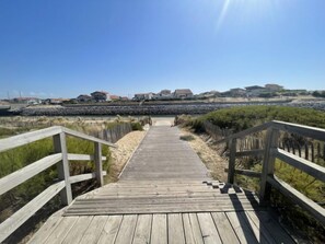Une promenade en bois qui mène à une plage, avec des maisons en arrière-plan.