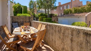 Une terrasse avec une table ronde et des chaises, un mur en pierre et une vue sur des bâtiments et des arbres.