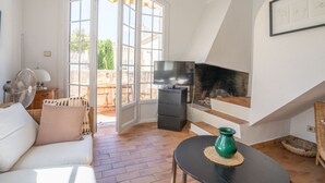 Un salon comprenant un canapé, un téléviseur, une cheminée et donnant sur une terrasse extérieure grâce à de grandes portes vitrées.