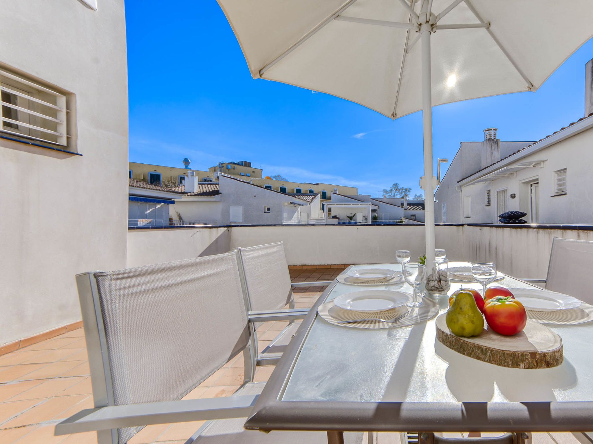 A rooftop terrace with a table set for two, surrounded by chairs, under a large umbrella.