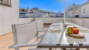 A rooftop terrace with a table set for two, surrounded by chairs, under a large umbrella.