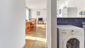 A laundry room with a Samsung washing machine, a dining area with wooden chairs, and a kitchen with blue tiles.